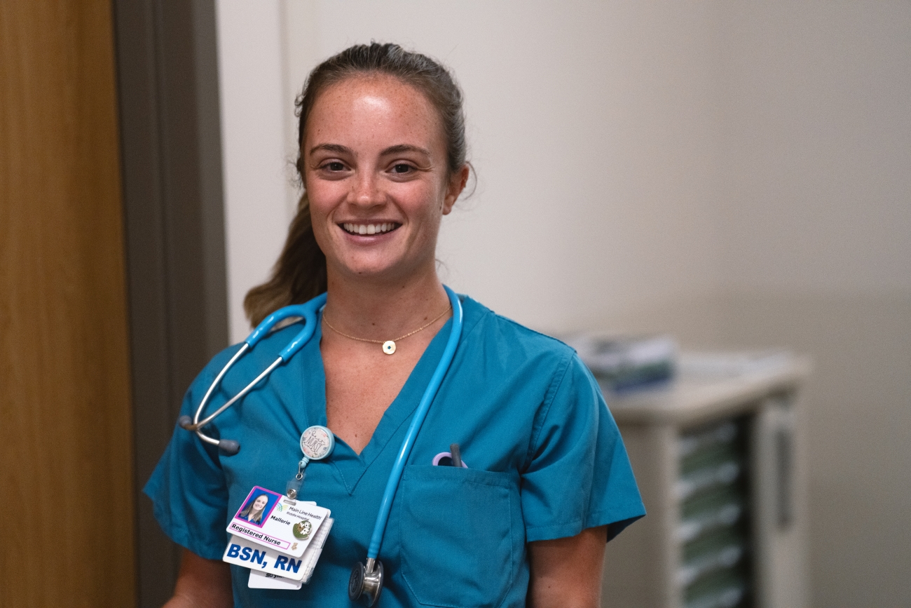 A smiling nurse wearing teal scrubs and a stethoscope stands indoors, with a hospital badge and "BSN, RN" visible. A medical cart is in the background.